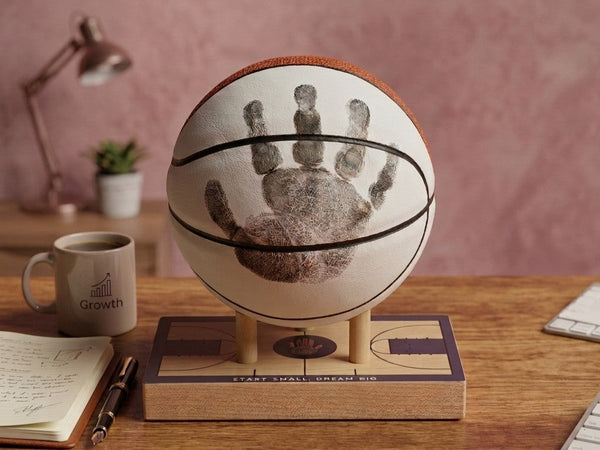 A child's handprint preserved on a display-quality basketball, mounted on a maple display base